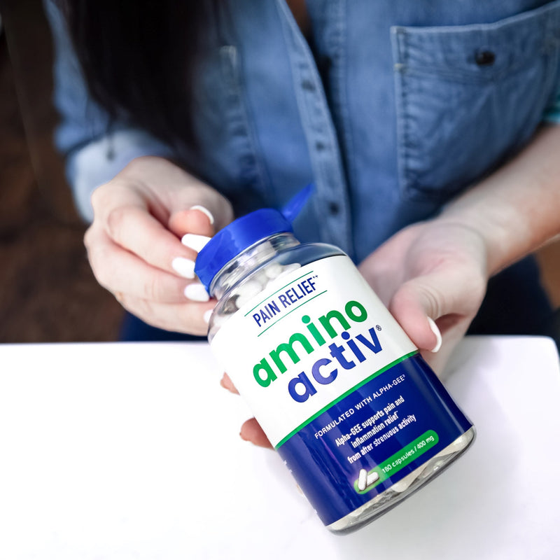 Person holding a bottle of Amino Activ supplement on a white surface