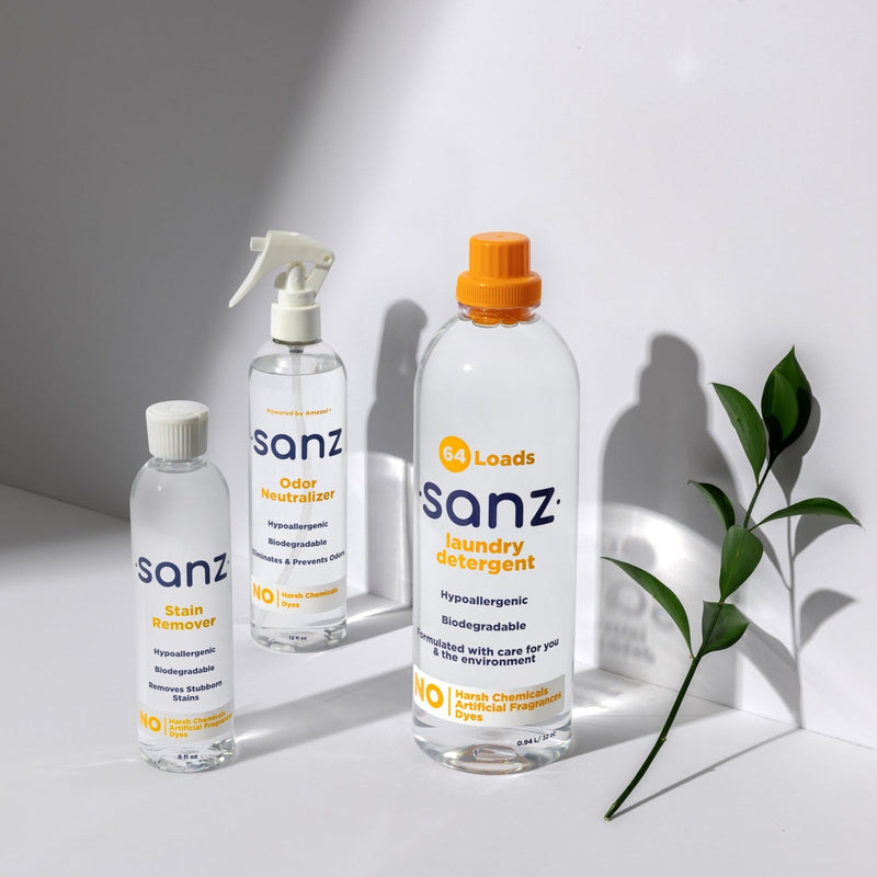 Three bottles of Sanz laundry detergent on a light background with a plant.